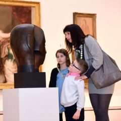 A mother with two young children admire a wooden head sculpture