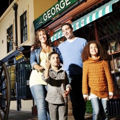Two adults and two children on a recreated Victorian street. One child is pointing at something.