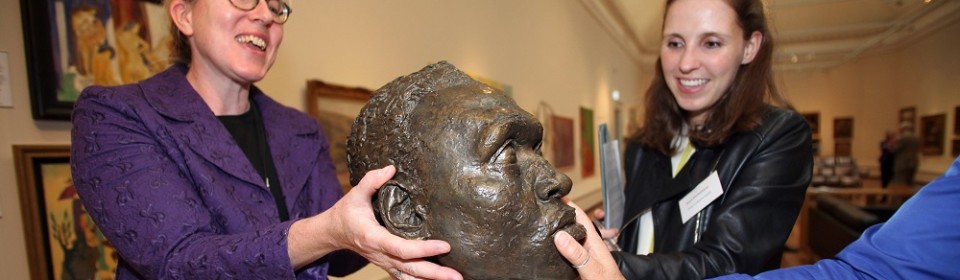 Three people placing their hands on the statue of a head.