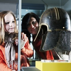 A young girl and woman look at the York Helmet on display