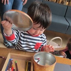 A male toddler opens the lid of a tin to reveal colouring pencils