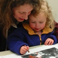 A female toddler sits with a female adult drawing