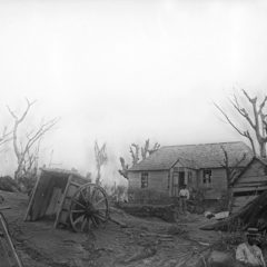 Black and white photo of house with bare trees and a half-buried cart