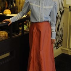 Woman in Victorian style blue blouse and red skirt in museum interior