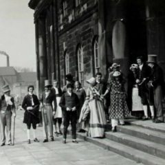 Men and women in Victorian costume on stone steps outside 17th century building