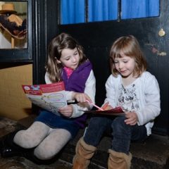 Two girls sat on a step in a museum completing a trail