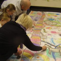 Two adults and two children drawing on a giant sheet of paper