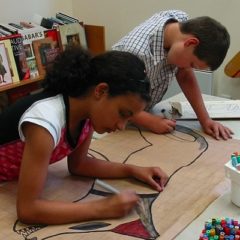 A girl and boy draw a colourful horse on brown paper