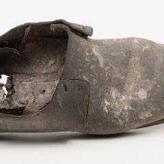 A man's leather shoe which has been lent on its side. The shoe's heel is broken.