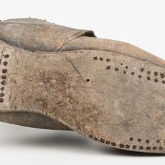 A man's leather shoe which has been lent on its side. The shoe is broken at the heel.