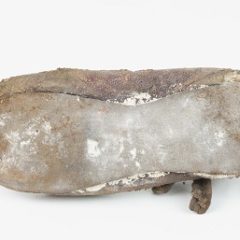 A child's leather shoe, which has been lent on its side. The shoe is very worn.