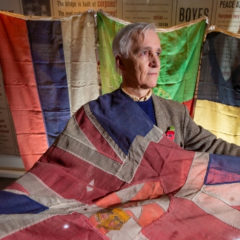 A man holding an historic flag and stood in front of three other historic flags.