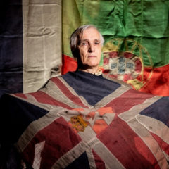 A man holding an historic flag and stood in front of two other historic flags.