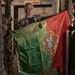 A man stood in a replica trench holding an historic flag.