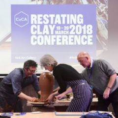 Three artists moving a piece of pottery. The pottery is in front of a projector screen.
