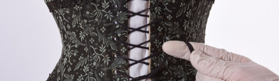 A pair of gloved hands tying the lace on a black corset.