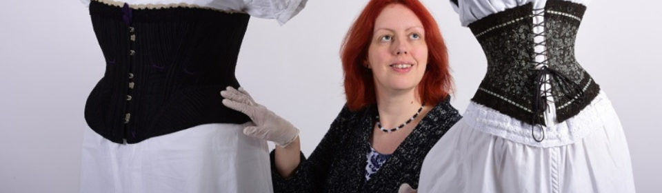 A woman placing her white-gloved hands on two mannequins. The mannequins are wearing old-fashioned women's clothing.