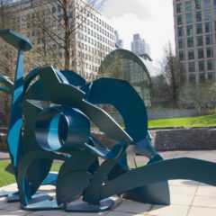 A blue sculpture in an outdoor space. The sculpture is made up of different shaped pieces.