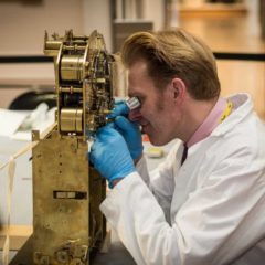 A man wearing blue gloves examining a gold machine.