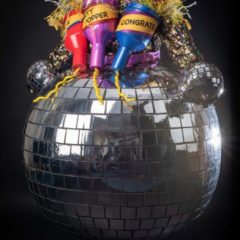 A glitterball dress with three giant party poppers stuck to it, one which says 'congrats'.