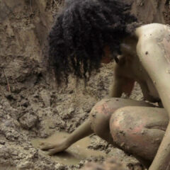 A naked woman crouched in the mud