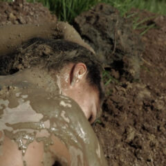 a woman lies in the mud with mud covering her naked back